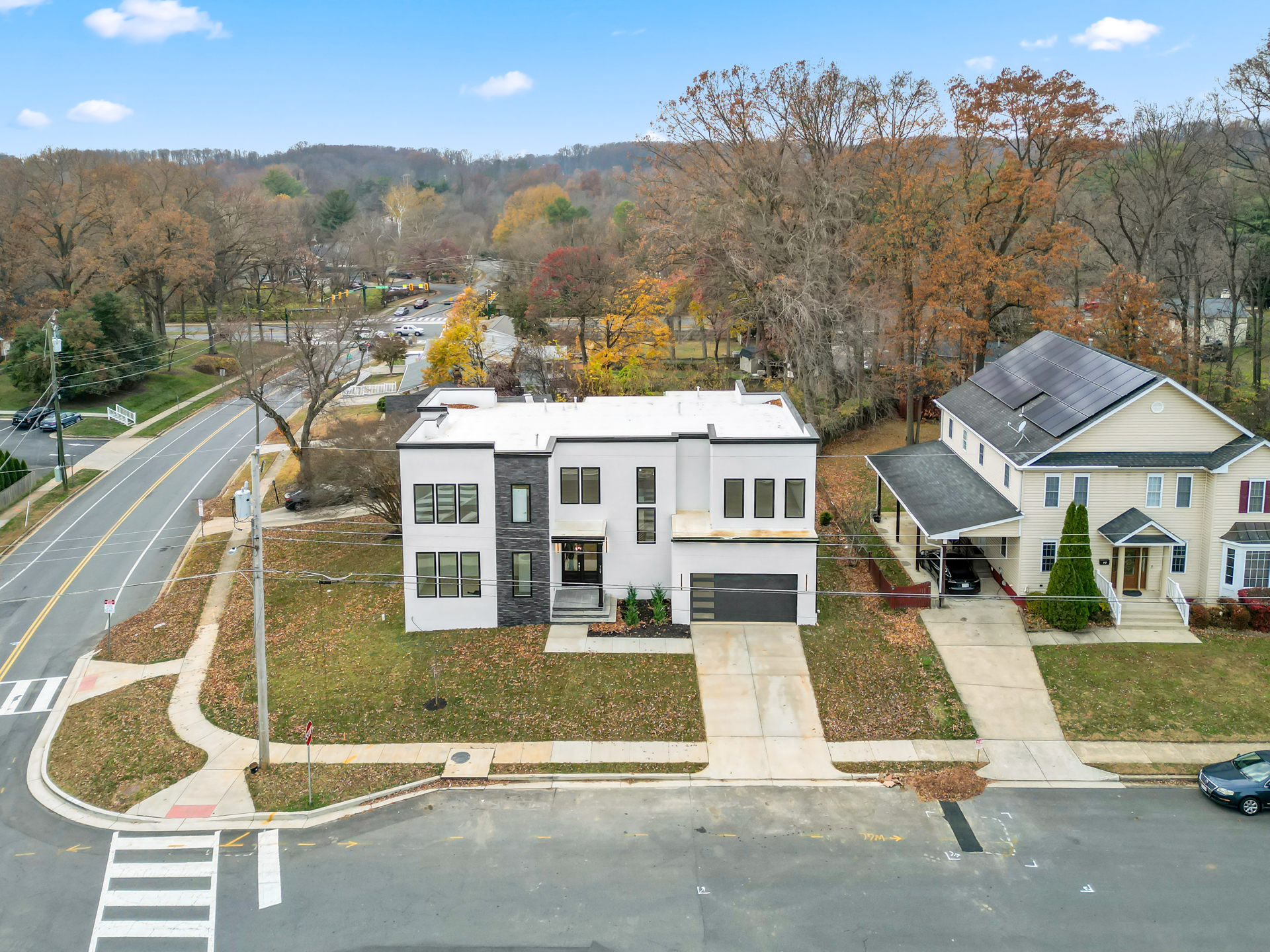 An aerial drone view of a modern two-story home on a tree-lined residential street
