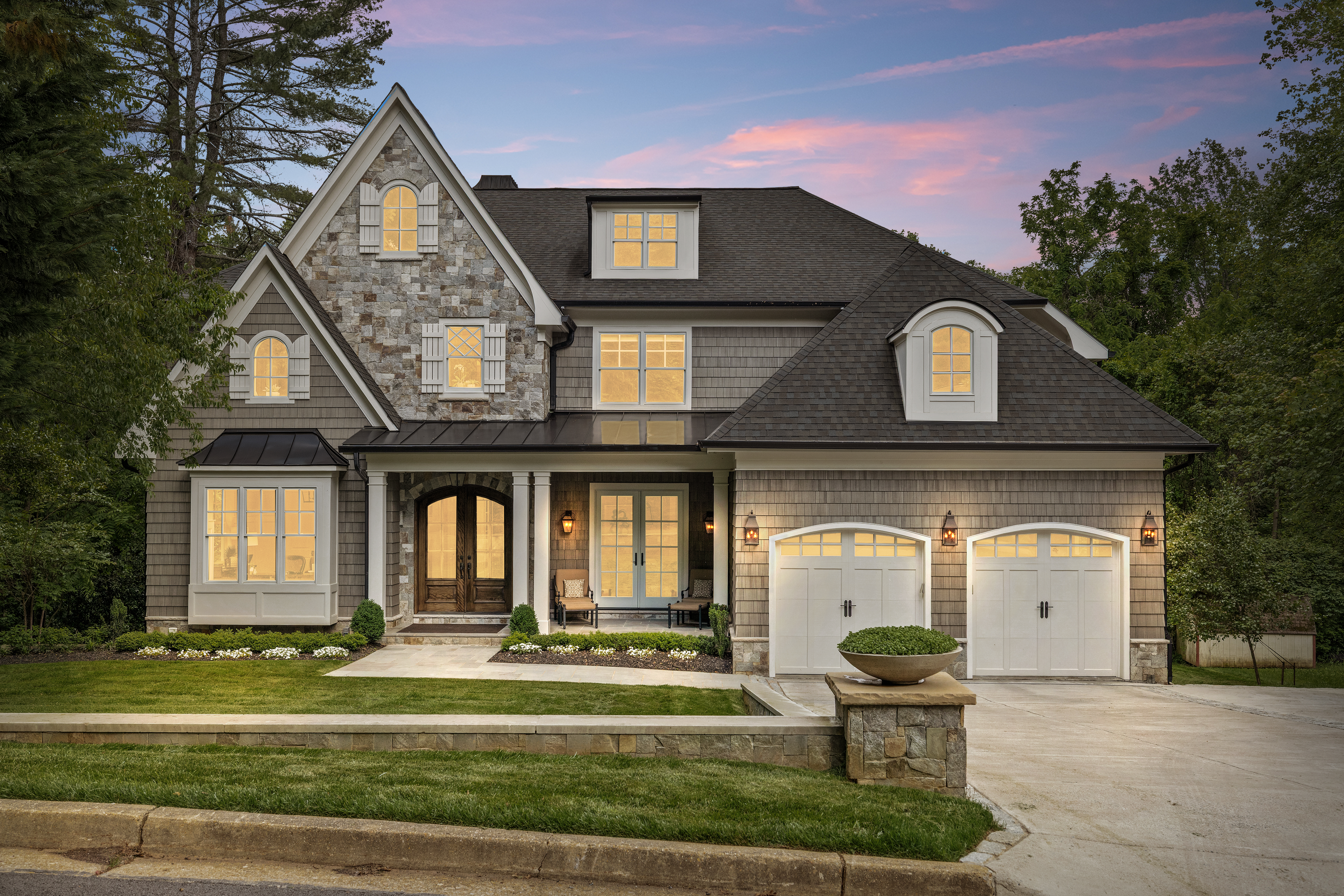 Luxury stone-and-shingle home photographed at dusk with glowing windows and a pink twilight sky