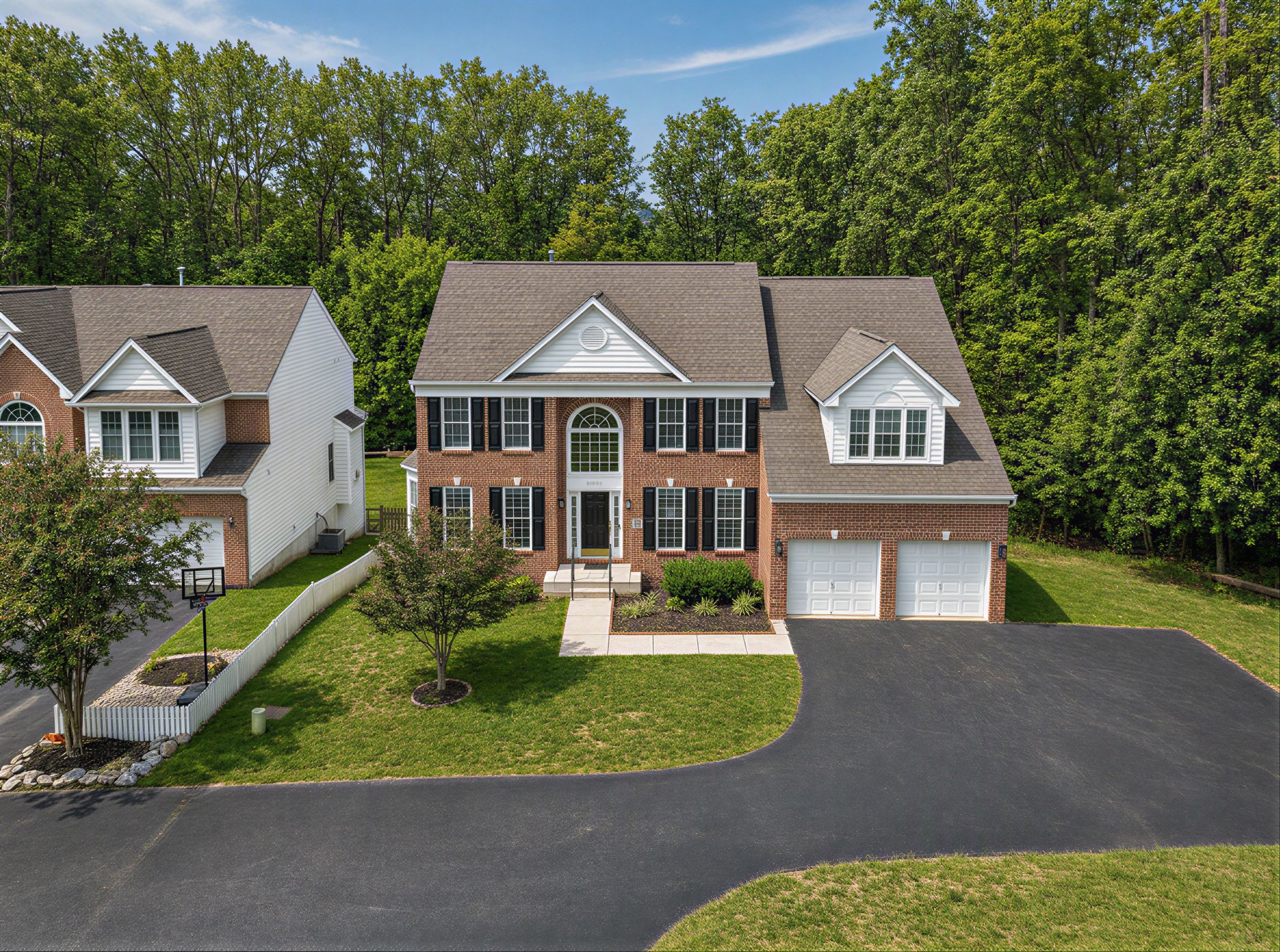 Drone view of a brick colonial home, driveway, and manicured lot from above