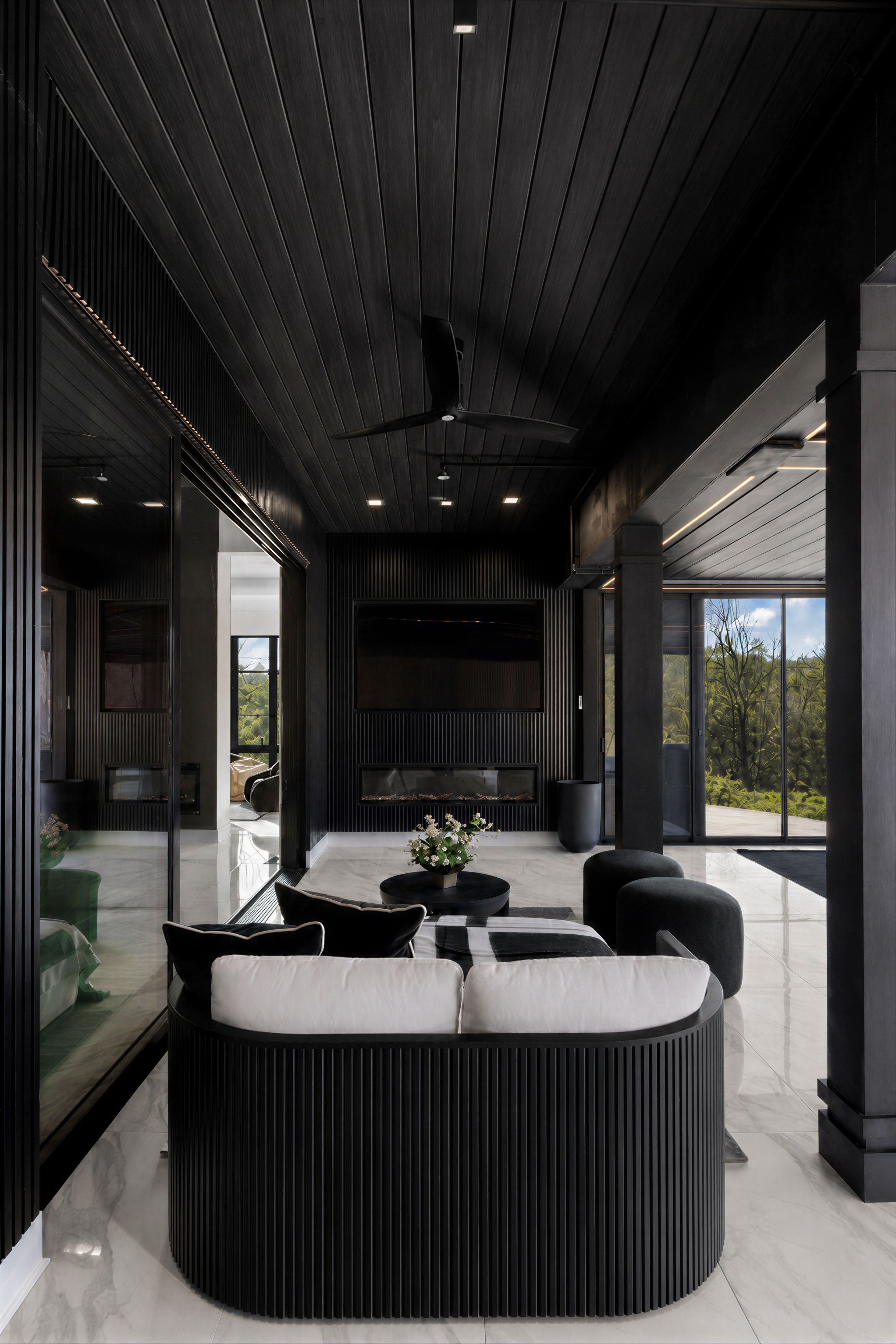 Dark, moody lounge with black slat ceiling, round seating, and dramatic lighting