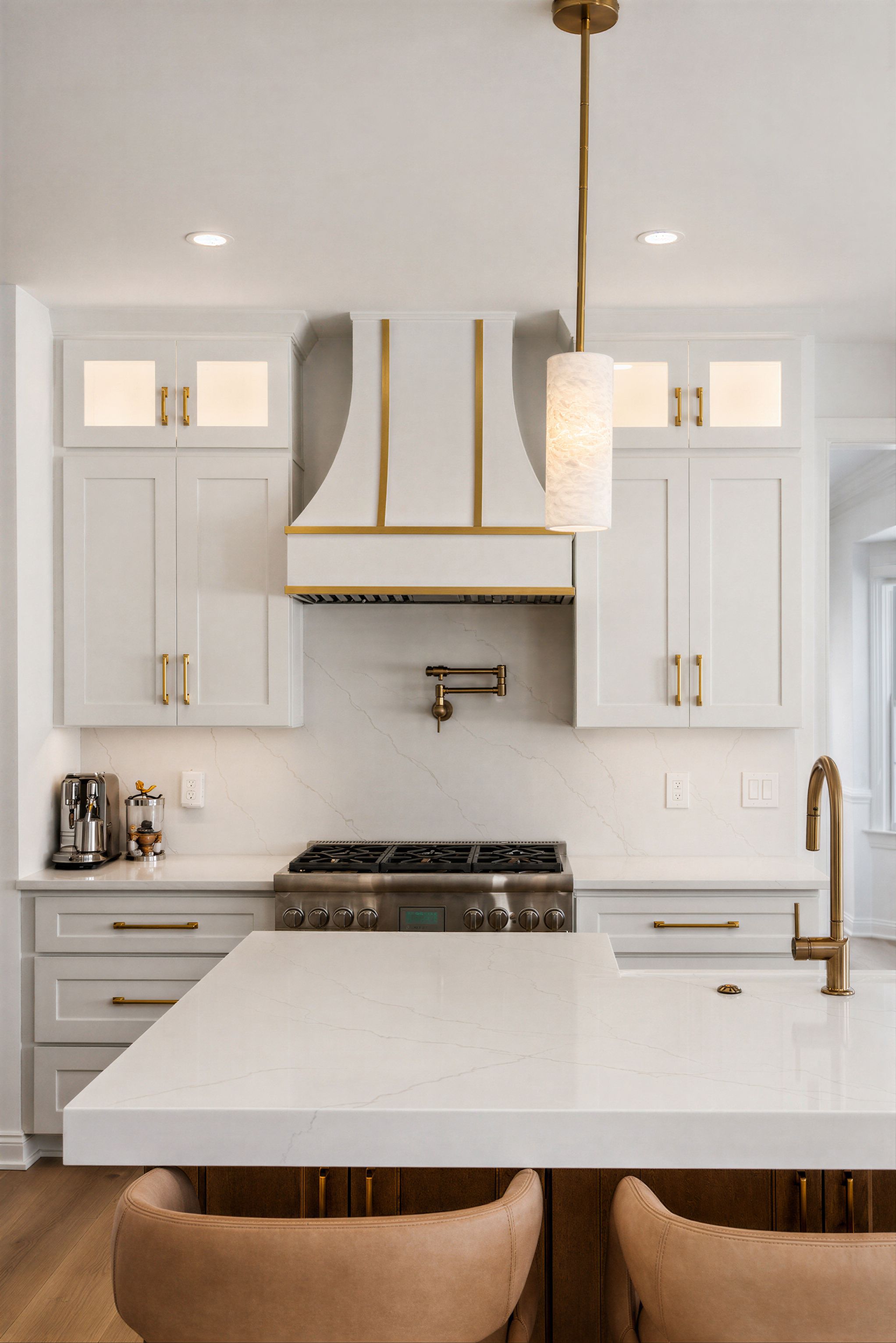 White kitchen with brass-trimmed range hood, quartz island, and upholstered stools